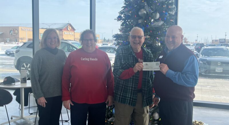 ae3c99_b7ba10ede70b4bf3ba0e78aab6a67912~mv2-min Group of people holding a check in front of a christmas tree